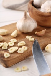 Photo of Aromatic cut garlic, cloves and bulbs on white wooden table, closeup
