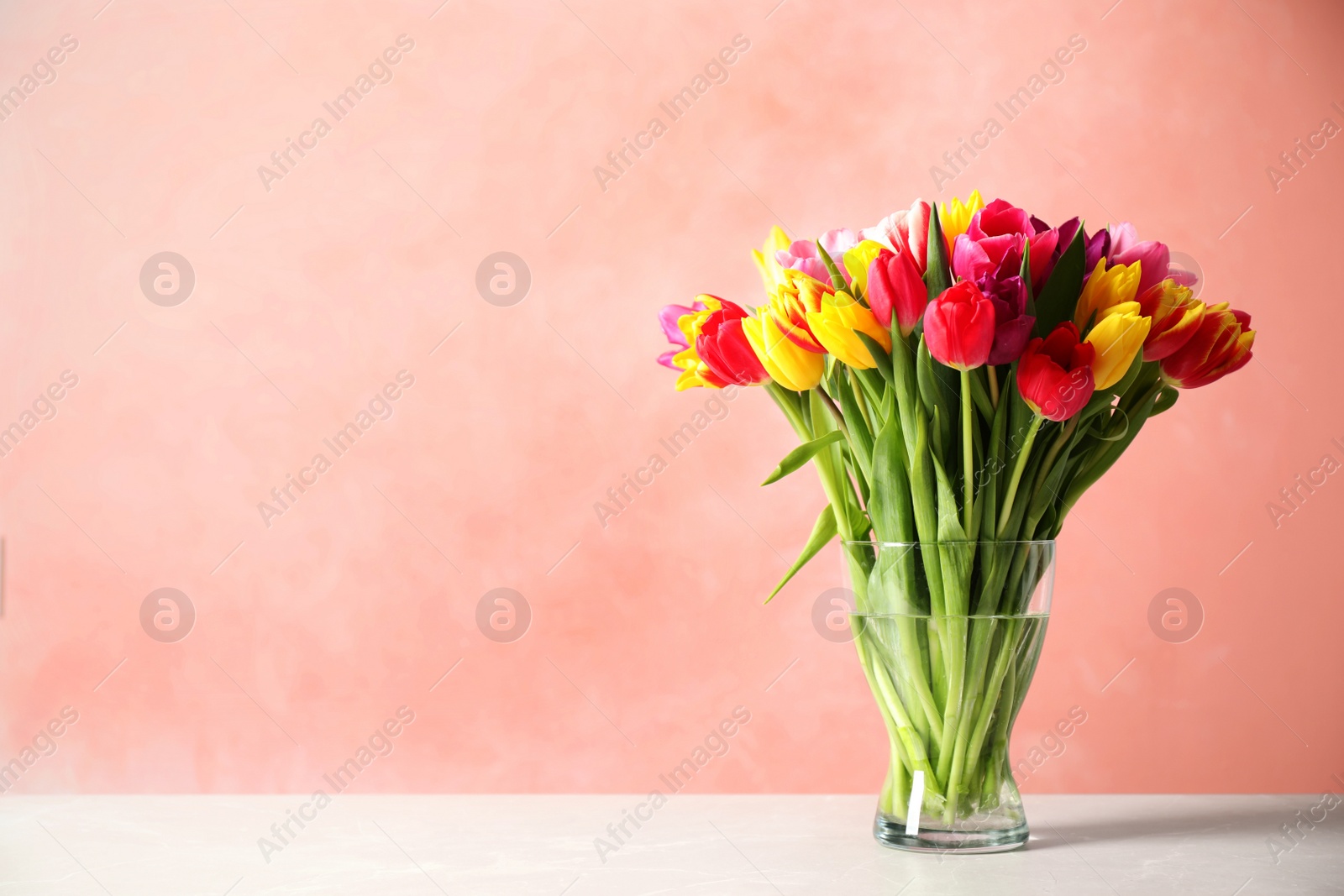 Photo of Beautiful spring tulips in vase on table against light  pink background. Space for text