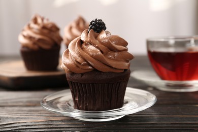 Photo of Delicious chocolate cupcake with cream and blackberry on black wooden table, closeup