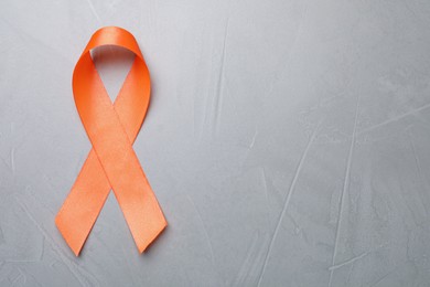 Orange ribbon on light grey table, top view with space for text. Multiple sclerosis awareness