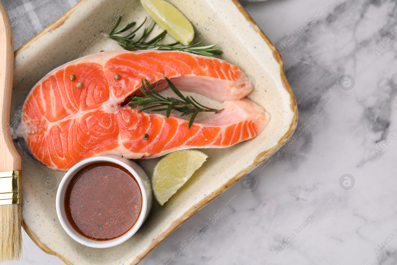 Photo of Fresh fish, lime, rosemary and marinade in baking dish on light marble table, top view. Space for text