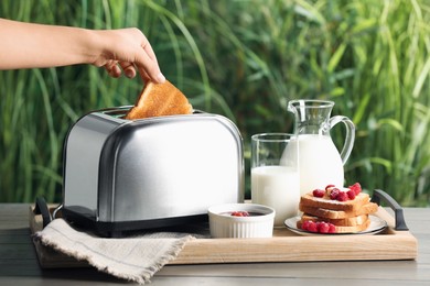 Photo of Woman taking roasted bread out of toaster at wooden table, closeup