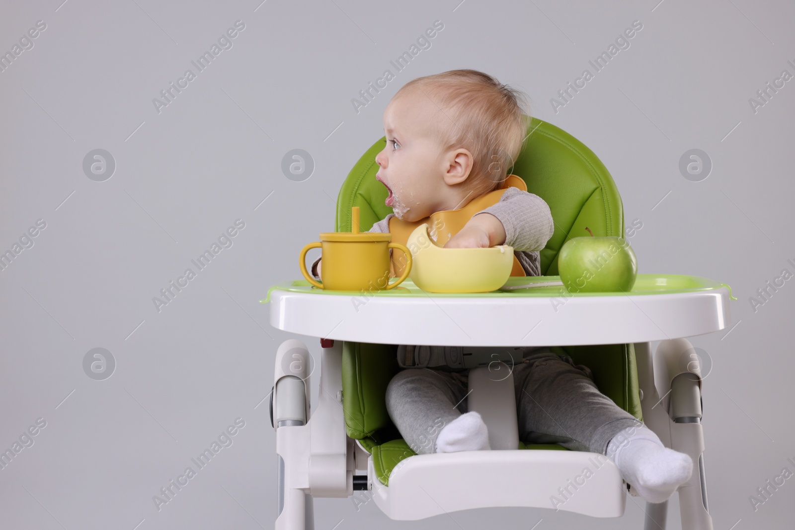 Photo of Cute little baby eating healthy food in high chair on gray background, space for text