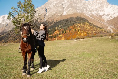 Photo of Young woman with horse in mountains on sunny day, space for text. Beautiful pet