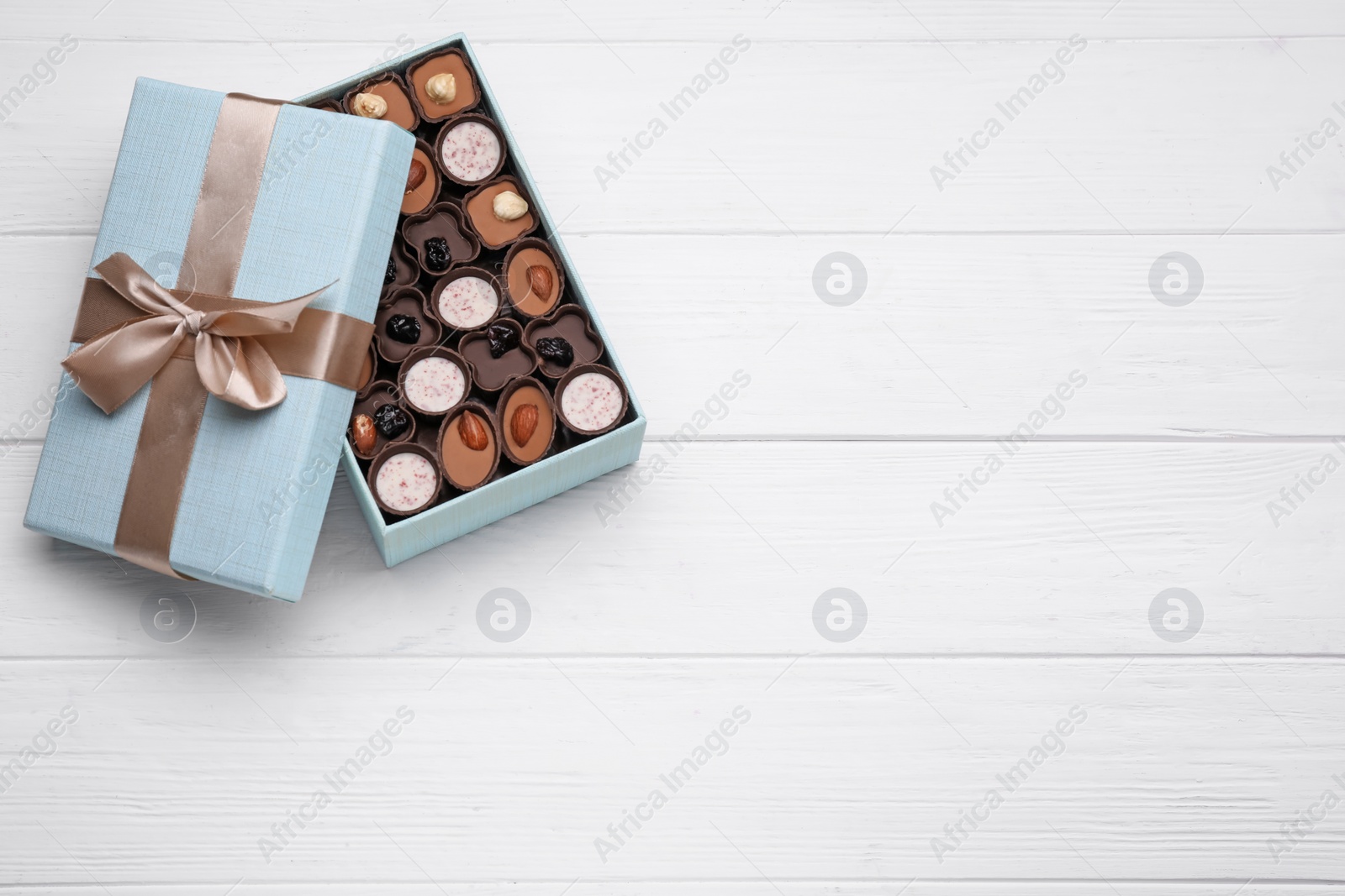 Photo of Open box of delicious chocolate candies on white wooden table, top view. Space for text