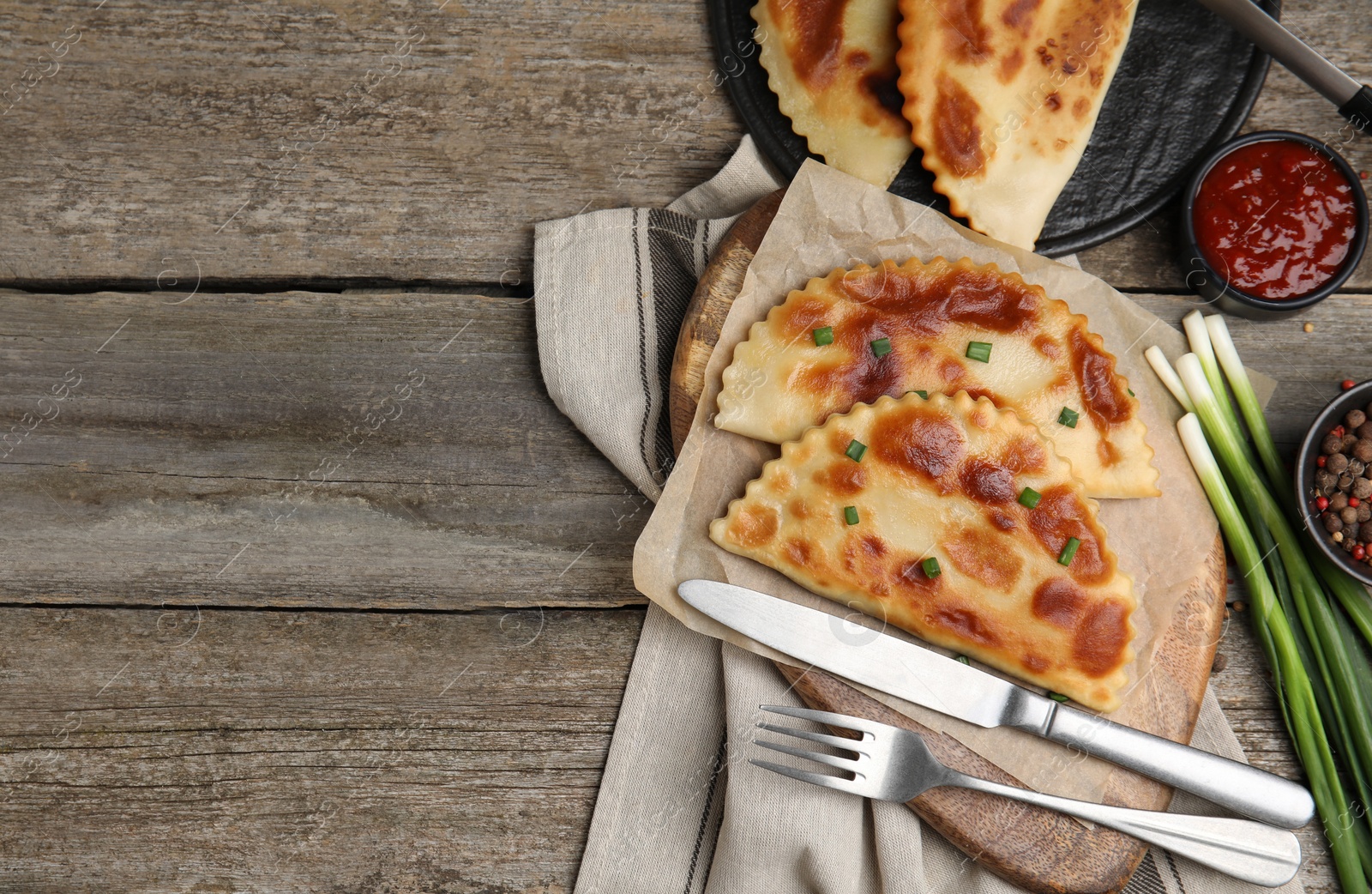 Photo of Delicious fried chebureki with ketchup and onion served on wooden table, flat lay. Space for text