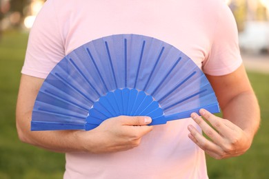 Photo of Man with blue hand fan outdoors, closeup