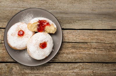 Photo of Delicious donuts with jelly and powdered sugar on wooden table, top view. Space for text