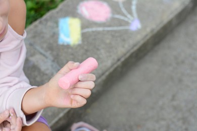 Photo of Little child chalk piece sitting on curb outdoors, closeup. Space for text