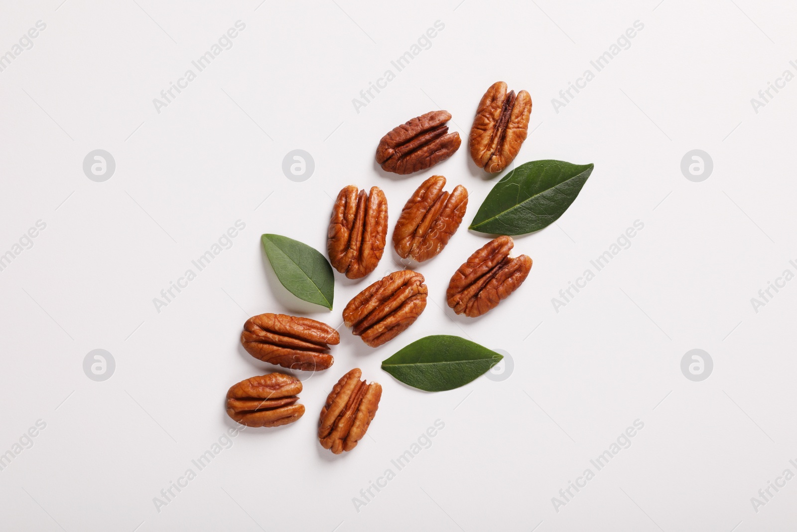 Photo of Delicious pecan nuts and green leaves on white background, flat lay