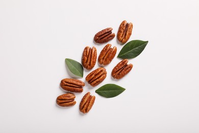 Delicious pecan nuts and green leaves on white background, flat lay