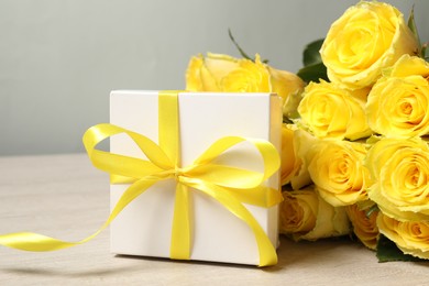 Beautiful bouquet of yellow roses and gift box on wooden table, closeup