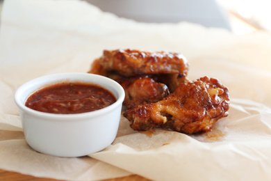 Photo of Delicious chicken wings with sauce on wooden board, closeup