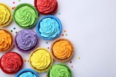 Many tasty cupcakes with bright cream and sprinkles on white background, flat lay. Space for text