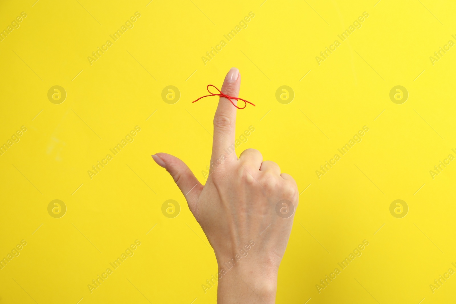 Photo of Woman showing index finger with tied red bow as reminder on yellow background, closeup