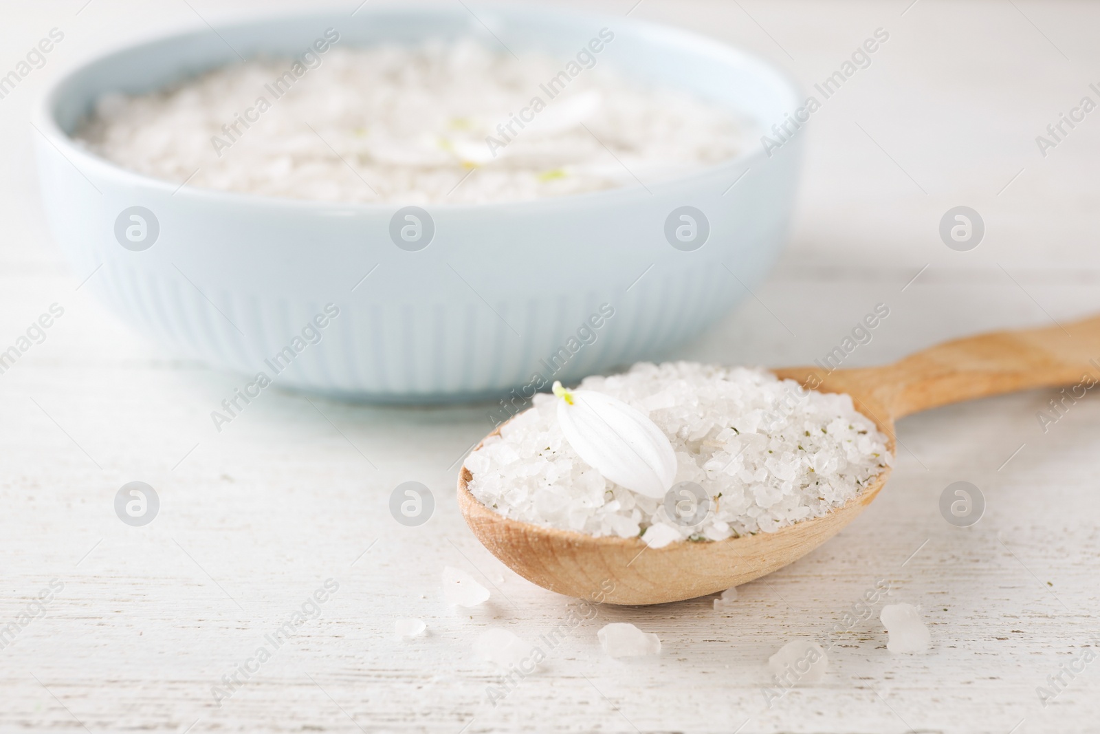 Photo of Spoon with sea salt for spa scrubbing procedure and petal on wooden table