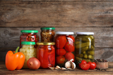 Glass jars with different pickled vegetables on wooden table