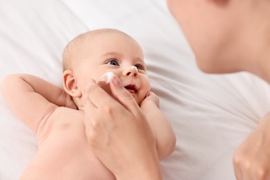 Photo of Woman applying cream onto baby`s face on bed, closeup