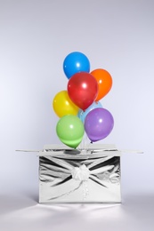 Photo of Gift box with bright air balloons on light background