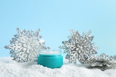 Photo of Jar of hand cream and decorative snowflakes on snow against light blue background. Winter skin care