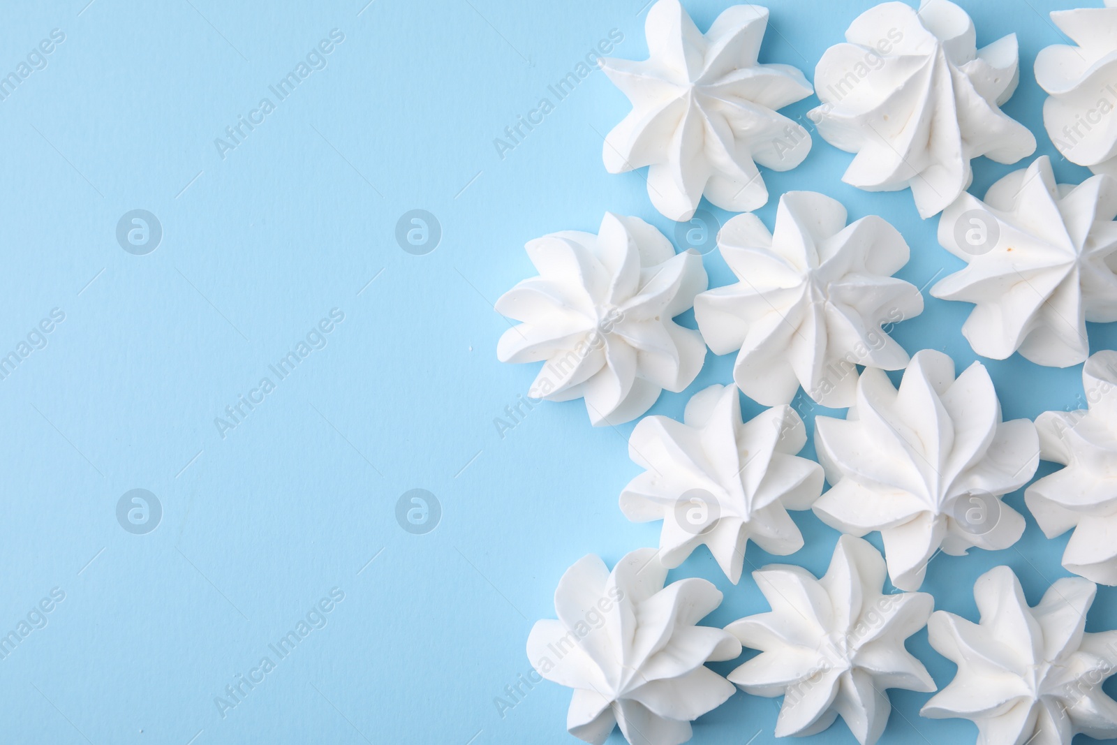 Photo of Tasty meringue cookies on light blue background, flat lay. Space for text