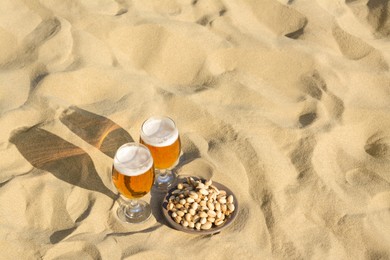 Glasses of cold beer and pistachios on sandy beach, space for text