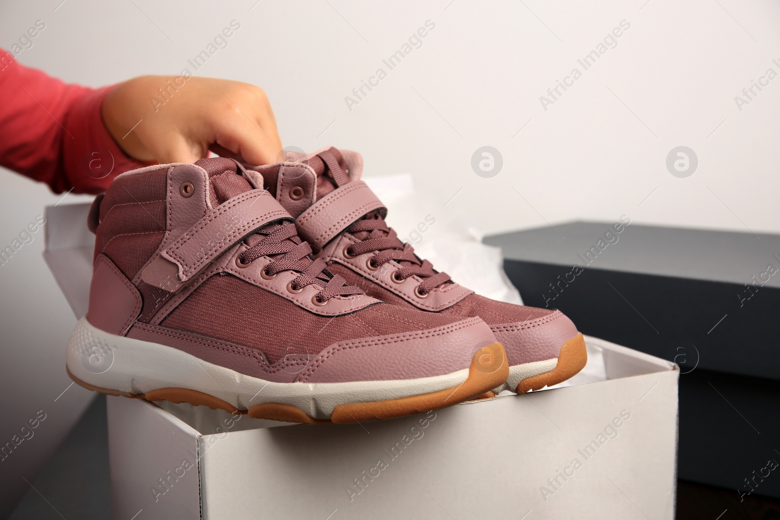 Photo of Girl taking out new sneakers from box against light grey background, closeup