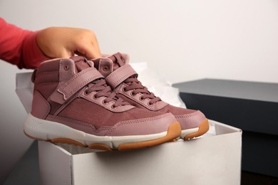 Girl taking out new sneakers from box against light grey background, closeup