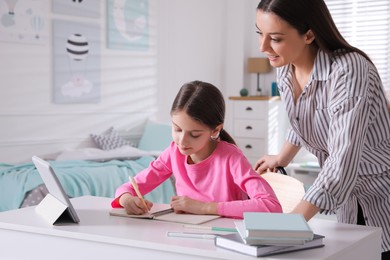 Mother helping her daughter doing homework with tablet at home