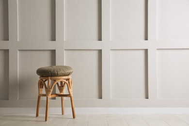 Stylish wooden stool with cushion near white wall, space for text. Interior element