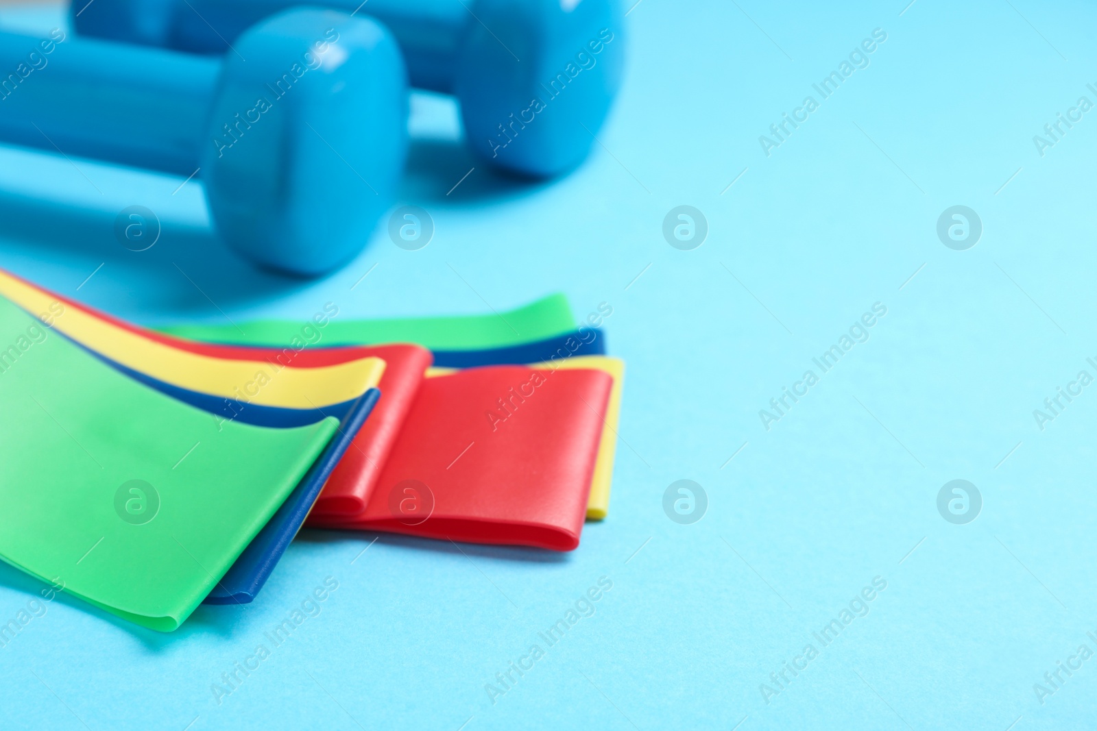 Photo of Fitness elastic bands and dumbbells on light blue background, closeup. Space for text