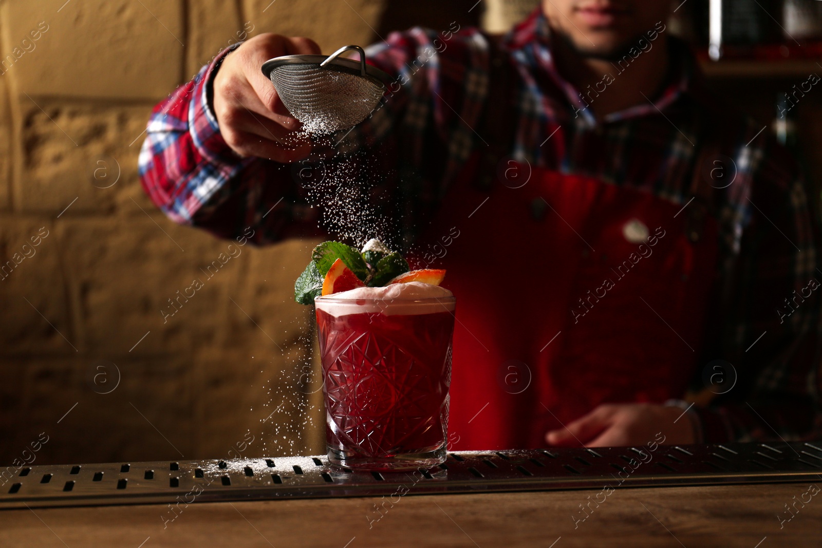 Photo of Bartender decorating glass of fresh alcoholic cocktail at bar counter, closeup