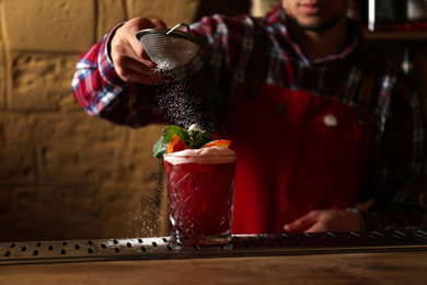 Photo of Bartender decorating glass of fresh alcoholic cocktail at bar counter, closeup