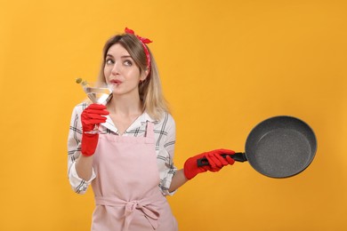 Photo of Young housewife with frying pan and glass of martini on yellow background