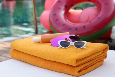 Beach towels, sunglasses and sunscreen on sunbed near outdoor swimming pool. Luxury resort