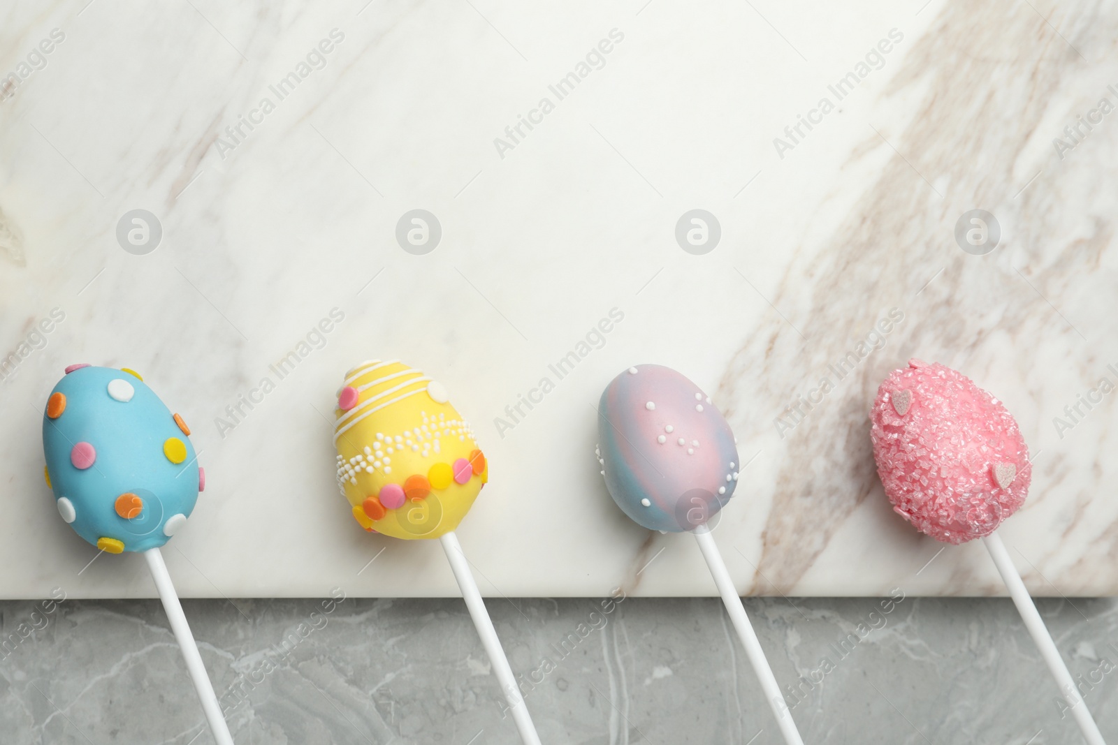 Photo of Egg shaped cake pops and space for text on grey marble table, flat lay. Easter celebration