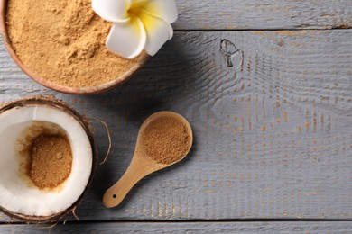 Photo of Coconut sugar, bowl, spoon, flower and fruit on grey wooden table, flat lay. Space for text