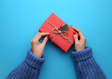 Woman holding Christmas gift box on light blue background, top view