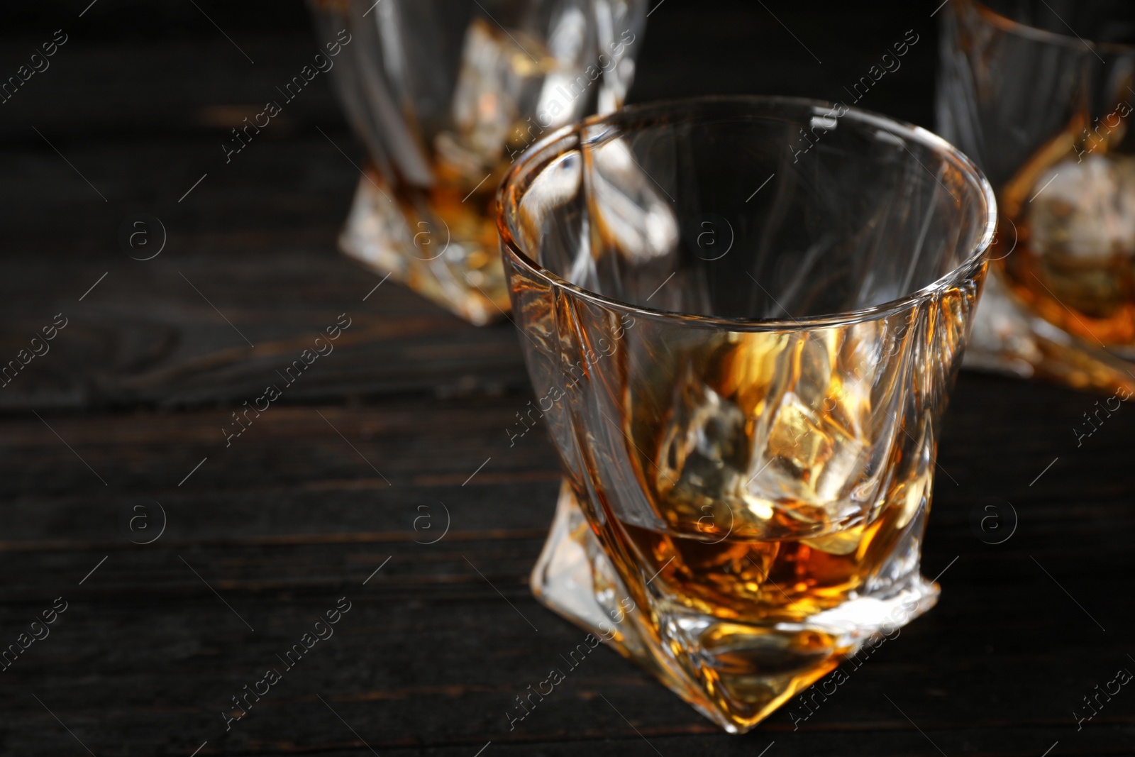 Photo of Golden whiskey in glass with ice cubes on wooden table. Space for text