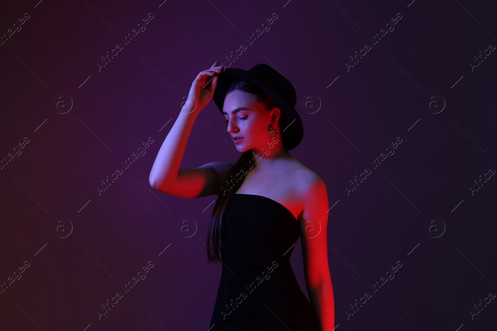 Photo of Portrait of beautiful young woman in hat on color background with neon lights