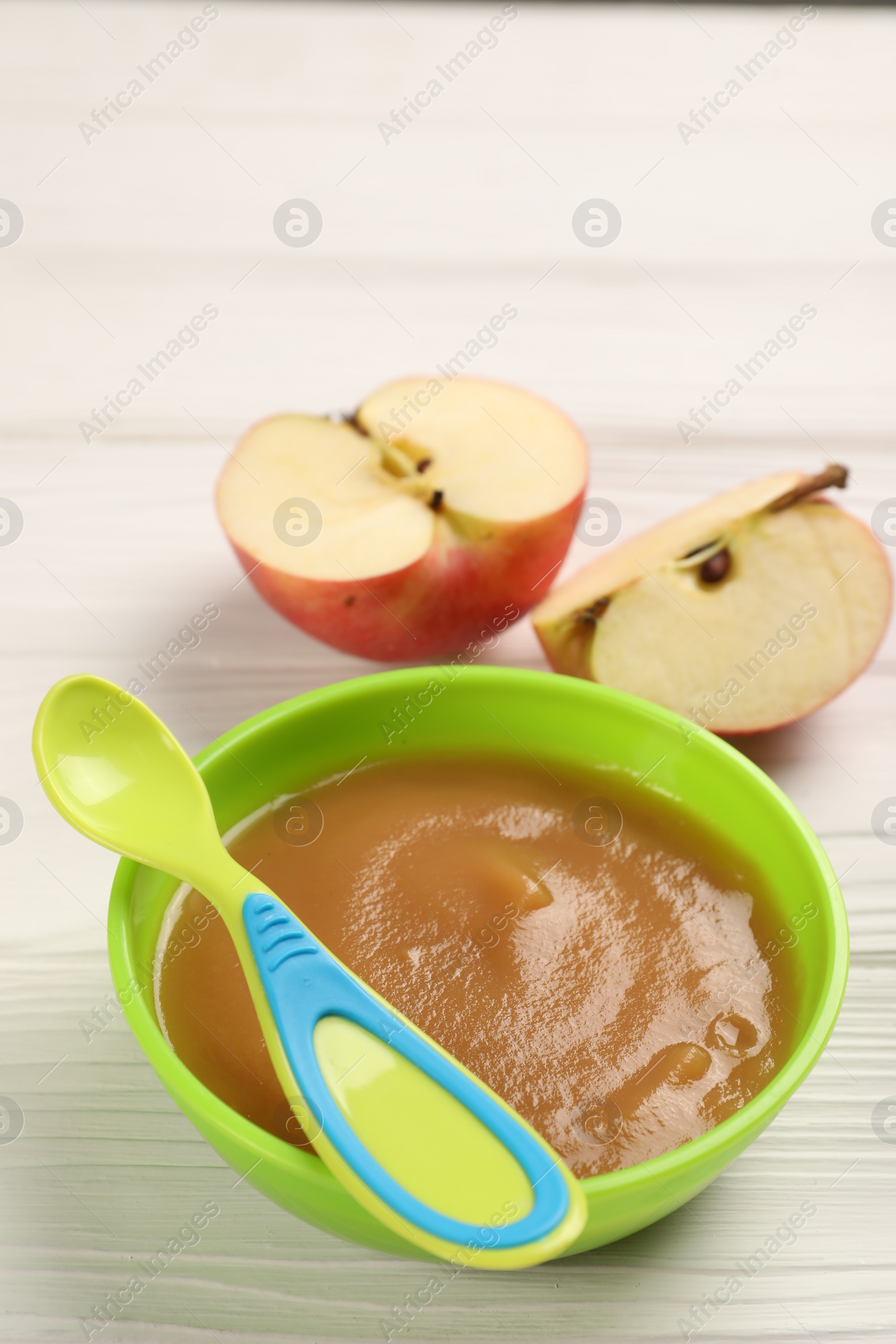 Photo of Baby food. Puree of apples in bowl and spoon on white wooden table