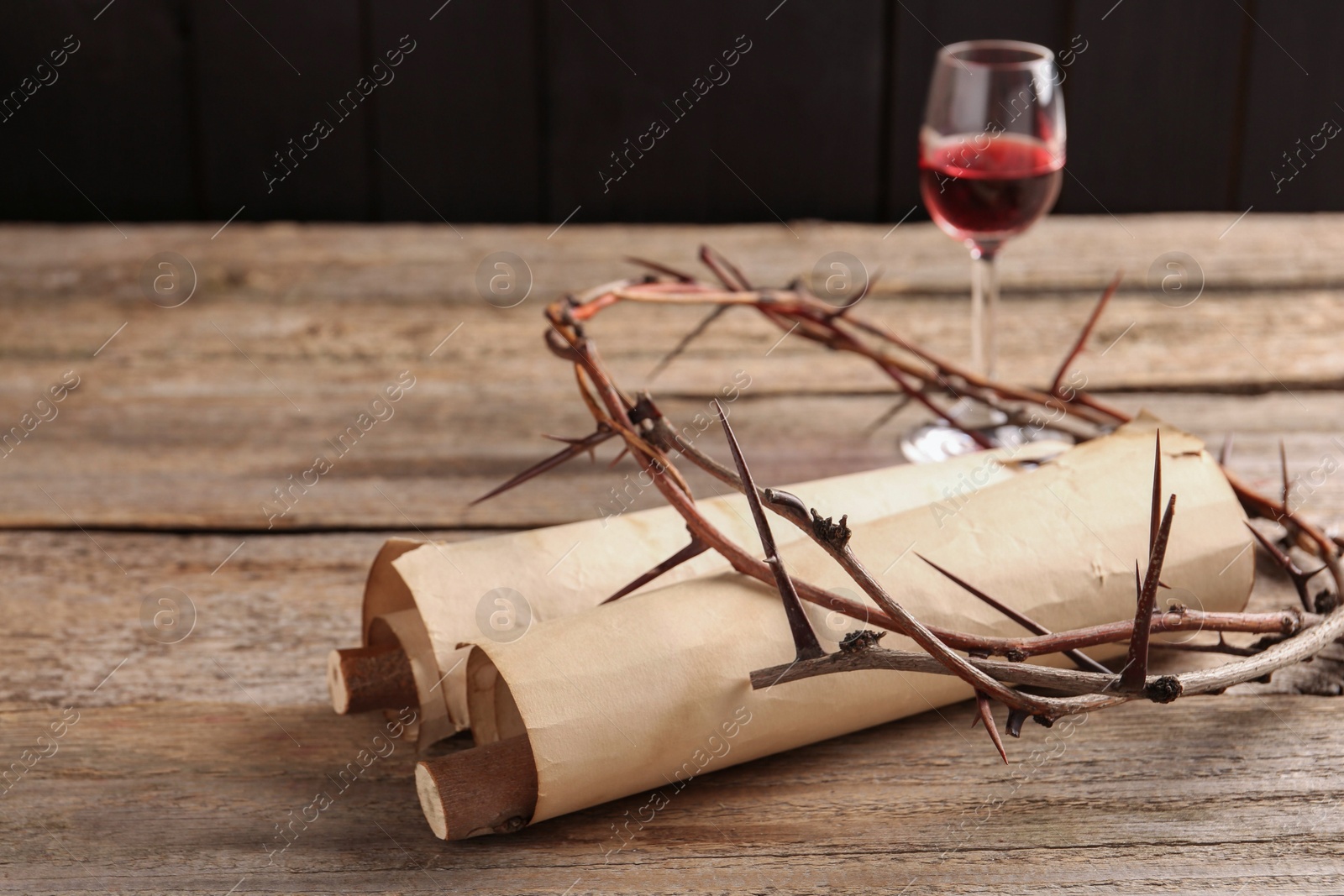 Photo of Crown of thorns, old scrolls and glass with wine on wooden table, selective focus