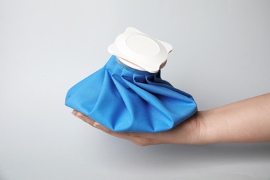 Photo of Woman holding ice pack against light background, closeup