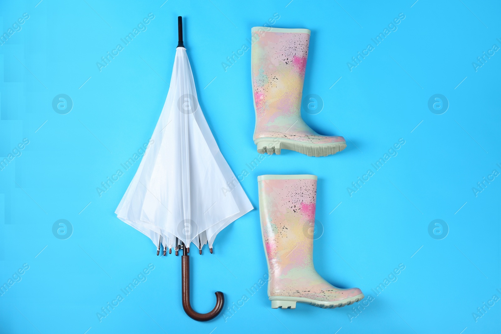 Photo of Beautiful white umbrella and rubber boots on blue background, flat lay