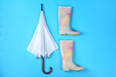 Photo of Beautiful white umbrella and rubber boots on blue background, flat lay