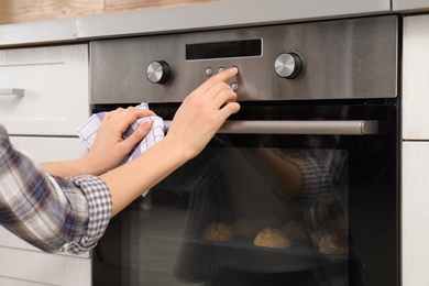 Photo of Young woman adjusting oven settings in kitchen, closeup