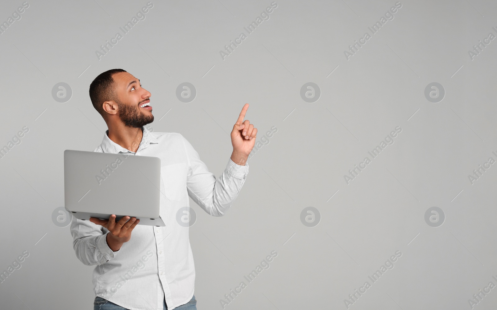 Photo of Smiling young man with laptop on grey background, space for text