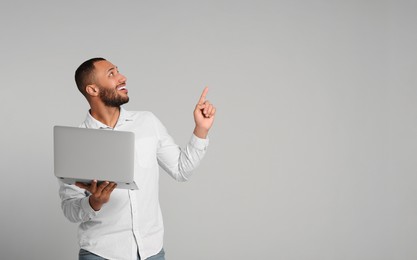 Photo of Smiling young man with laptop on grey background, space for text