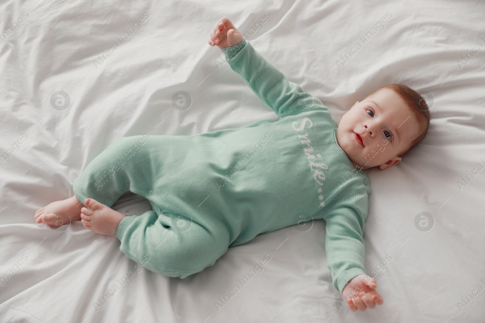 Photo of Cute little baby lying on bed with soft white blanket, above view