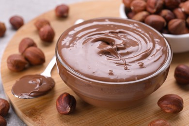 Photo of Bowl with tasty chocolate paste and nuts on wooden board, closeup